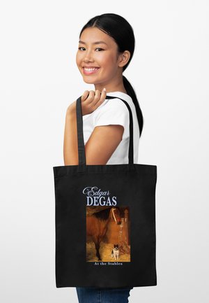 Usmívající se žena držící černou tašku s malbou Edgara Degase zobrazující koně a psa ve stáji, světlé pozadí.