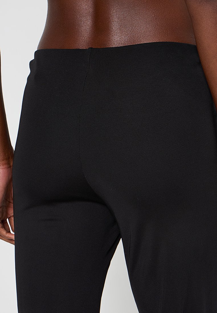 Leggings neri a vita alta con una superficie liscia e elastica, caratterizzati da un design semplice e senza chiusure o dettagli visibili.