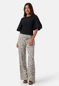 Zwarte textuurtop met pofmouwen, gecombineerd met hoge, wijde leeuwenspots broek in grijs en beige. G gedragen met zwarte sandalen met bandjes.