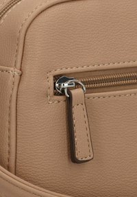 Matériau synthétique texturé marron clair avec une poche zippée, dotée de quincaillerie en argent et d'une tirette en cuir avec des détails de couture.