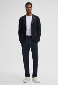Marineblazer aus strukturiertem Stoff über einem weißen T-Shirt, kombiniert mit schmal geschnittenen Marine-Hosen und weißen Sneakers. Schlichtes, modernes Design.