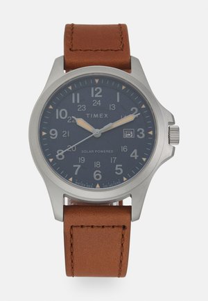 Timex Solar-Uhren mit einem dunkelblauen Zifferblatt, einem silbernen Edelstahlgehäuse und einem braunen Lederarmband. Verfügt über eine Datumsanzeige und auffällige Ziffern.