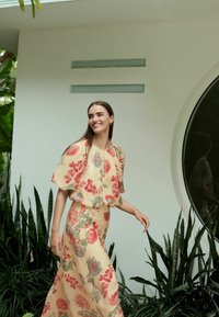 Zweiteiliges Outfit mit floralem Muster, das einen gelben Hintergrund mit roten und blauen Blumen bietet; leichtes Material, lockere Passform und kurze Ärmel.