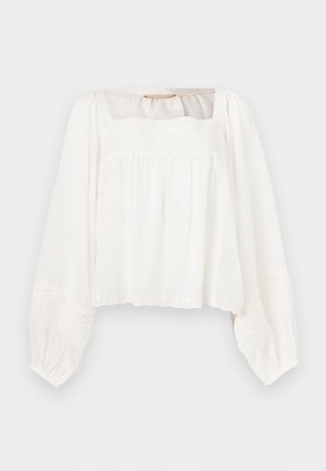 Blouse blanche à manches longues avec encolure carrée, coupe ample, et délicats détails floraux brodés sur la poitrine, les poignets et l'ourlet.
