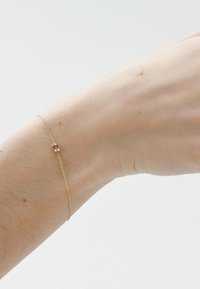 Pulsera delicada de cadena de oro con un pequeño colgante que presenta gemas rojas y transparentes en la muñeca de una persona.