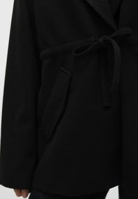 Must-haves on musta vööga mantel, millel on sile tekstuur, šalli krae ja küljetasku. Disain sisaldab seotud vööd, mis tagab vormika välimuse.