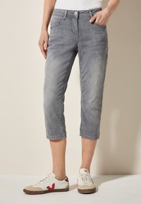 Pantalones cortos de mezclilla gris claro, con cinco bolsillos, cierre frontal con botón y una textura ligeramente deslavada. Usados con zapatillas blancas.