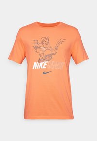 Oranssi Nike-t-paita, jossa on sarjakuvamainen tennis-pelaaja lyömässä palloa, "NIKE COURT" -teksti ja Nike-swoosh-logo edessä.