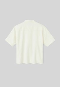 Chemise à manches courtes, col rabattu en tissu crème clair. Surface texturée avec une coupe décontractée. Détail de couture au niveau du dos. Pas de fermetures visibles.