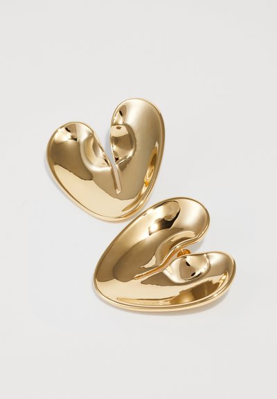 Clip per capelli in metallo dorato con un design ondulato a forma di cuore e una finitura lucida. Il clip presenta una superficie liscia e lucidata con forme curve.