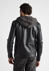 Černá kožená bunda se šedou látkovou kapucí, má hladkou texturu, přiléhavý střih a prošité detaily na zádech.