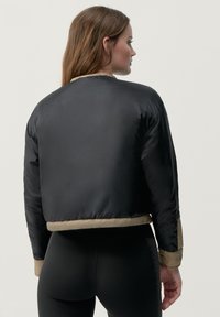 Avskuren puffjacka i svart med beige detaljer. Slätt, glänsande tyg; ribbade muddar och fåll; enkel design utan synlig hårdvara.