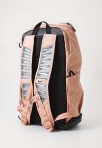 Mochila con un cuerpo de tela rosa, fondo negro y correas acolchadas que presentan un panel plateado texturizado. Incluye correas ajustables y bolsillos laterales.