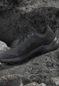 Black athletic shoe with textured sole resting on rough gray rocks in outdoor setting.