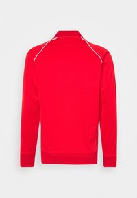 Červená mikina s vysokým límcem, dlouhými rukávy a bílým kontrastním švem podél ramen, vyrobená z hladké látky.