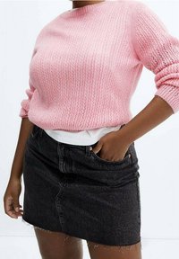 Rosa gestrickter Pullover mit gerippter Textur und aufgeschlagenen Ärmeln, kombiniert mit einem schwarzen Jeans-Minirock mit fransigem Saum und Fronttaschen.