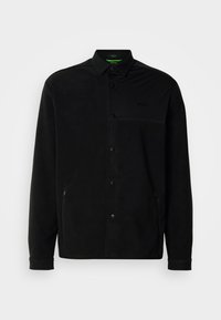 Casaco de fleece preto com colarinho pontudo, botões de pressão, bolsos laterais e detalhe do logótipo discreto no peito. Tecido leve e texturizado.