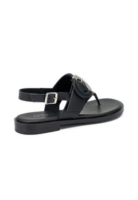 Sandalo in pelle nera con suola piatta, punta aperta e fascetta frontale con un accento circolare. Chiusura con fibbia sulla cinghia alla caviglia.