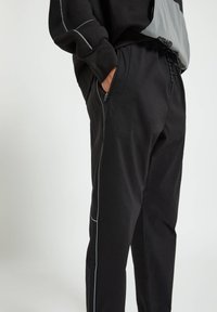 Svarta byxor med en något lös passform, med sidofickor, elastisk midja och kontrasterande grå piping längs sömmarna.