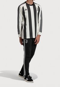 Juventus trøje med lange ærmer, sort og hvide lodrette striber, Adidas-logo på brystet, sorte sweatpants med hvide striber og sorte sko.