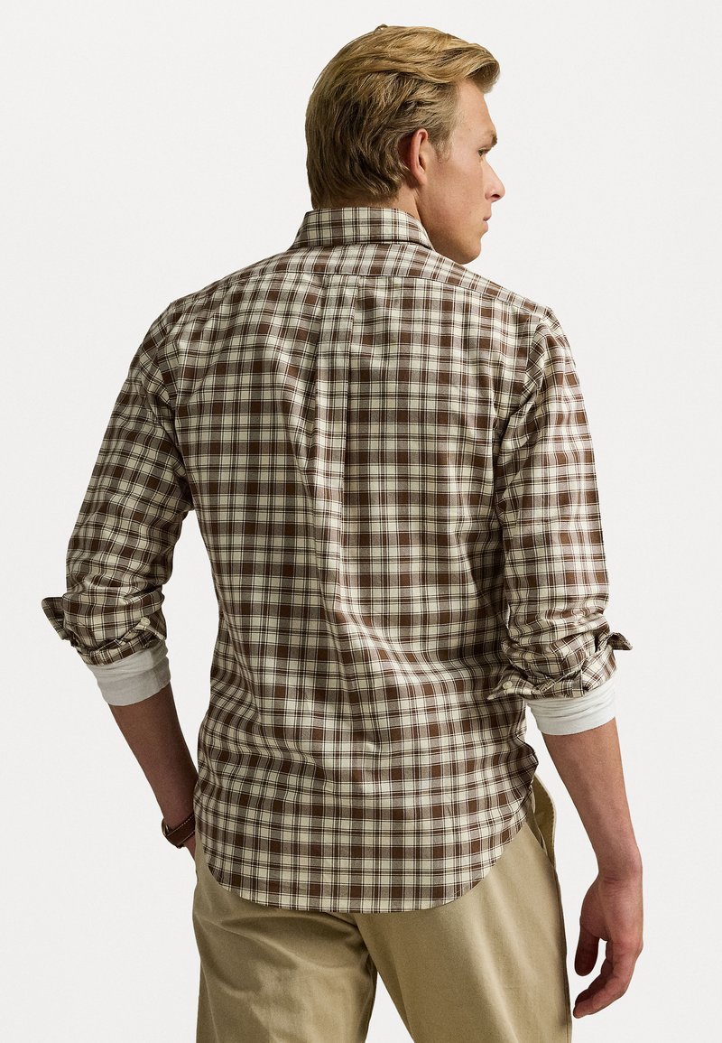 Camisa de cuadros marrón de botones con mangas enrolladas, que presenta un cuello y un dobladillo curvado, hecha de tejido tejido con una textura suave.