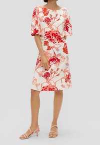 Blommig klänning med röda och rosa mönster på en ljus bakgrund. Kort ärm, rund halsringning och knälång fåll. Matchad med nude-hälar.