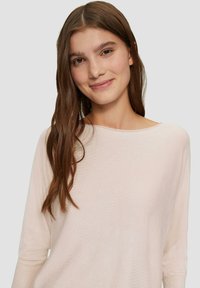 Helles pinkes Sweatshirt aus weichem, strukturiertem Stoff mit weitem Bootsausschnitt und dreiviertellangen Ärmeln, getragen von einem Modell mit langen Haaren.