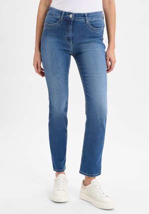Light blue denim jeans with a fitted silhouette, front pockets, a button closure, and white stitching details, paired with white sneakers.