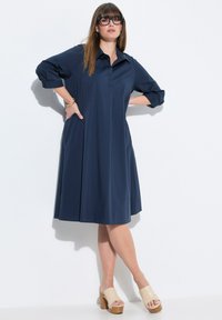 Marineblauwe jurk met kraag, driekwartmouwen en zijzakken; gecombineerd met platform sandalen. Soepele, lichte stof.