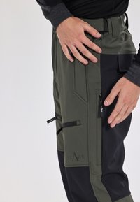 Groene en zwarte broek met een gladde textuur, voorzien van cargozakken, ritsen en een logo op het been. De taille heeft een verstelbare band.