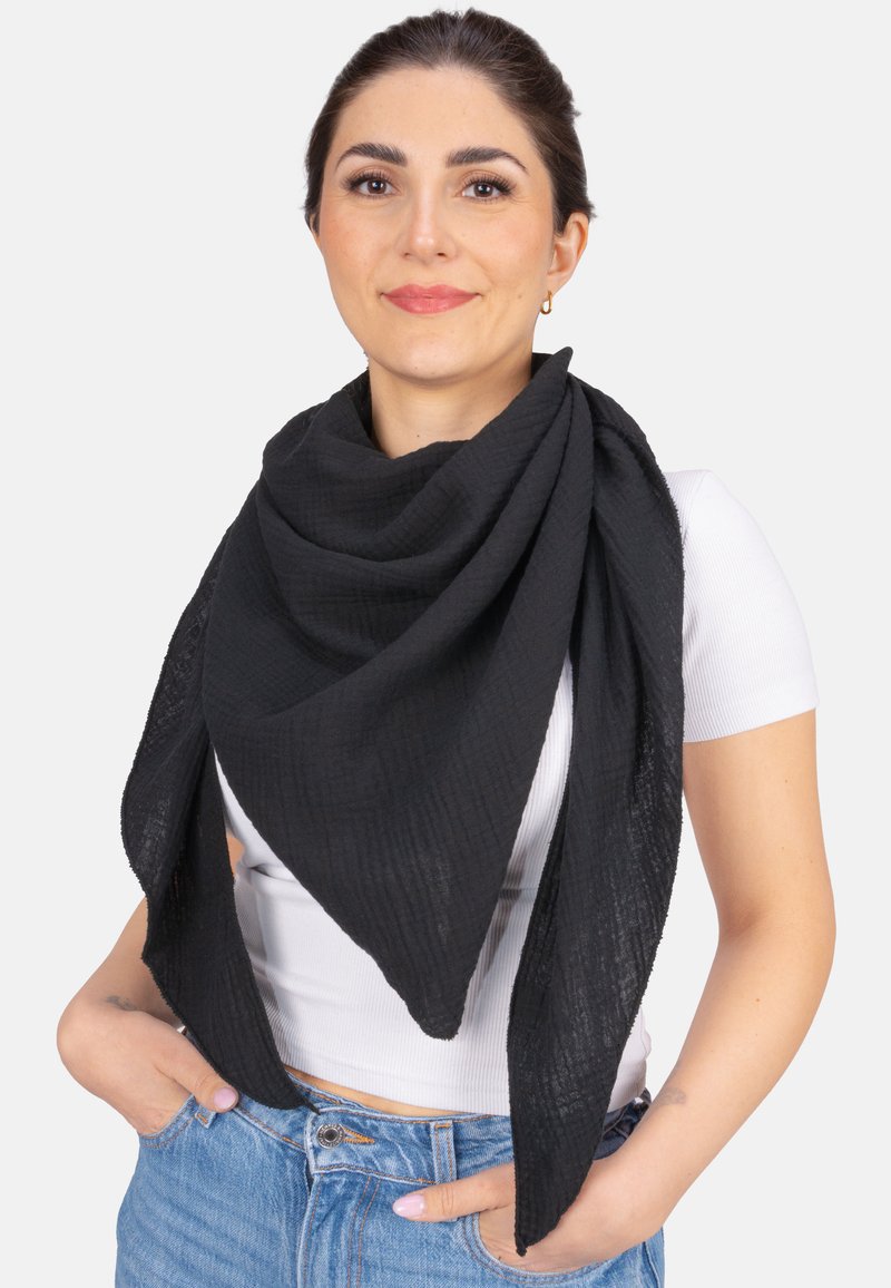 Écharpe noire en tissu texturé, drapée en forme triangulaire autour des épaules. Portée de manière décontractée sur un haut blanc.