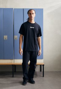 Black cotton T-shirt featuring "JUVENTUS" in white text, paired with black denim pants and black shoes, set against blue lockers.