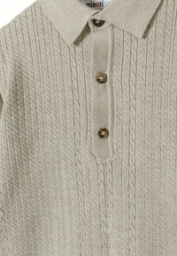 Beige gestricktes Poloshirt mit einer gerippten Textur, das einen Kragen hat und drei braune Knöpfe an der Vorderseite besitzt.