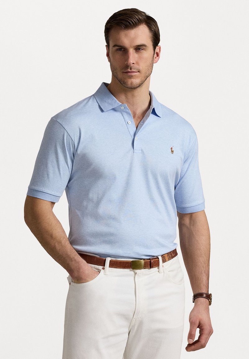 Rădăcină polo de culoare albastru deschis, dintr-un material moale, cu un guler cu trei butoni și mâneci scurte. Logo mic brodat pe piept. Asortat cu pantaloni albi.