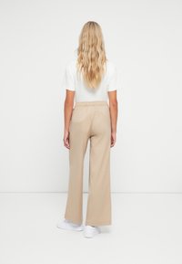 Beige brede benbukser med elastisk midjebånd, kombinert med en enkel hvit t-skjorte og hvite sneakers. Glatt stoff, avslappet passform.