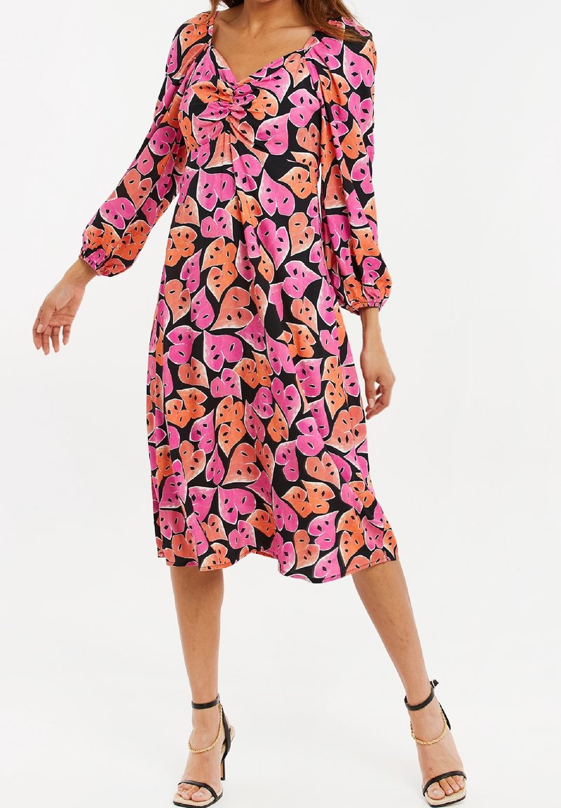 Sukienka z długim rękawem, sięgająca kolan, o czarnym tle z dużymi różowymi i pomarańczowymi wzorami liści. Teksturowana tkanina z marszczonym dekoltem.