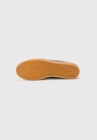 Suola di scarpa con grip in gomma arancione, caratterizzata da un motivo a spina di pesce, esposta su uno sfondo bianco uniforme.