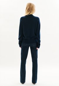Maglione lavorato a maglia color navy con orlo e polsini a costine, abbinato a jeans in denim scuro con gamba dritta e cuciture tono su tono. Sfondo neutro.