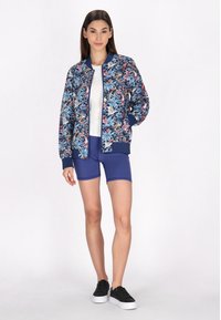 Giacca bomber navy con motivo floreale, caratterizzata da polsini e orlo a coste. Abbinata a un top bianco e shorts da ciclismo navy, insieme a sneakers nere.