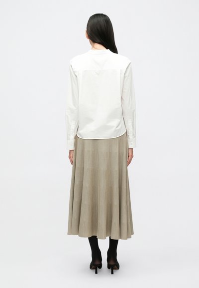 Λευκό πουκάμισο με μακριά μανίκια και στρογγυλή γραμμή στο τελείωμα, συνδυασμένο με μπεζ πλισέ μέσης μήκους φούστα. Μαύρες καλσόν και ψηλοτάκουνα παπούτσια ολοκληρώνουν το σύνολο.