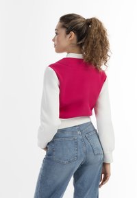 Tweedelige getailleerde jas met een roze voorkant en witte mouwen, voorzien van een kraag en ribgebreide manchetten, gecombineerd met hoge blauwe spijkerbroek.