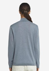 Jasnoniebieski sweter z długim rękawem i kołnierzykiem, o gładkiej strukturze, z prążkowanymi mankietami i dołem, przedstawiony na plecach modelki.