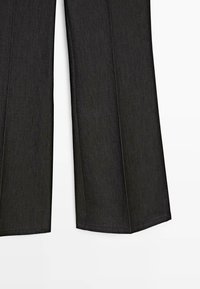 Pantalon large noir à coutures apparentes, tombant droit sur un fond blanc.