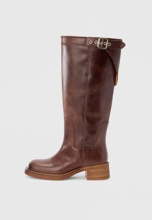 Cizme maro din piele până la genunchi, cu vârf rotund, toc bloc și detaliu cu cataramă în partea de sus. Textură netedă cu accente de cusături vizibile.