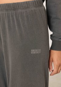 Artinantis asmuo dėvi pilkas elastinės juostos kelnes ir derančią ilgomis rankovėmis palaidinę, ant kelnių užrašyta „American Vintage“.