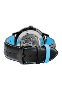 Montre en cuir noir avec perforations, doublure intérieure bleue et coutures contrastées. Boîtier transparent révélant les mécanismes intérieurs. Fermeture à boucle noire.