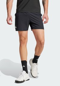 Schwarze Sportshorts mit strukturierter Oberfläche, versehen mit einem weißen Logo-Accent. Kombiniert mit weißen und schwarzen Sneakern sowie schwarzen Socken.
