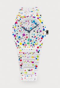 Montre en silicone colorée avec un bracelet blanc orné de points multicolores de différentes tailles. Cadran rond, aiguilles bleues et un design minimaliste.
