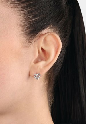 Silberne Ohrstecker in einem ineinander verschlungenen Knotendesign mit kleinen klaren Steinen. Glatte Textur mit hochglänzender Oberfläche.