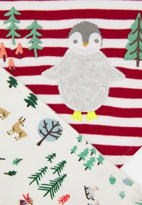 Aplique de pinguim cinza com pés amarelos em tecido listrado em vermelho e branco, combinado com um tecido branco que apresenta ilustrações de árvores e fauna.